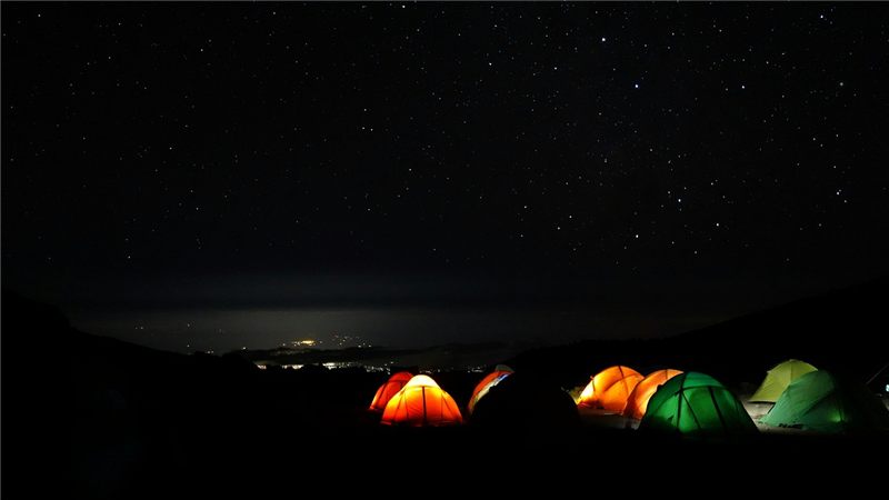 Illuminated mountain tents beneath a dark sky.