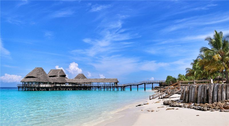 A white-sand Zanzibar beach with turquoise water and thatched buildings on stilts.