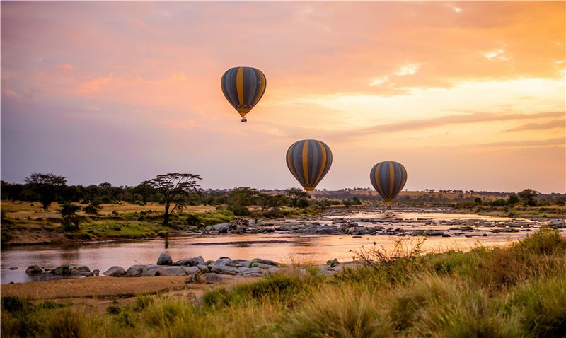 Hot air balloons over a river and open savannah at sunrise.